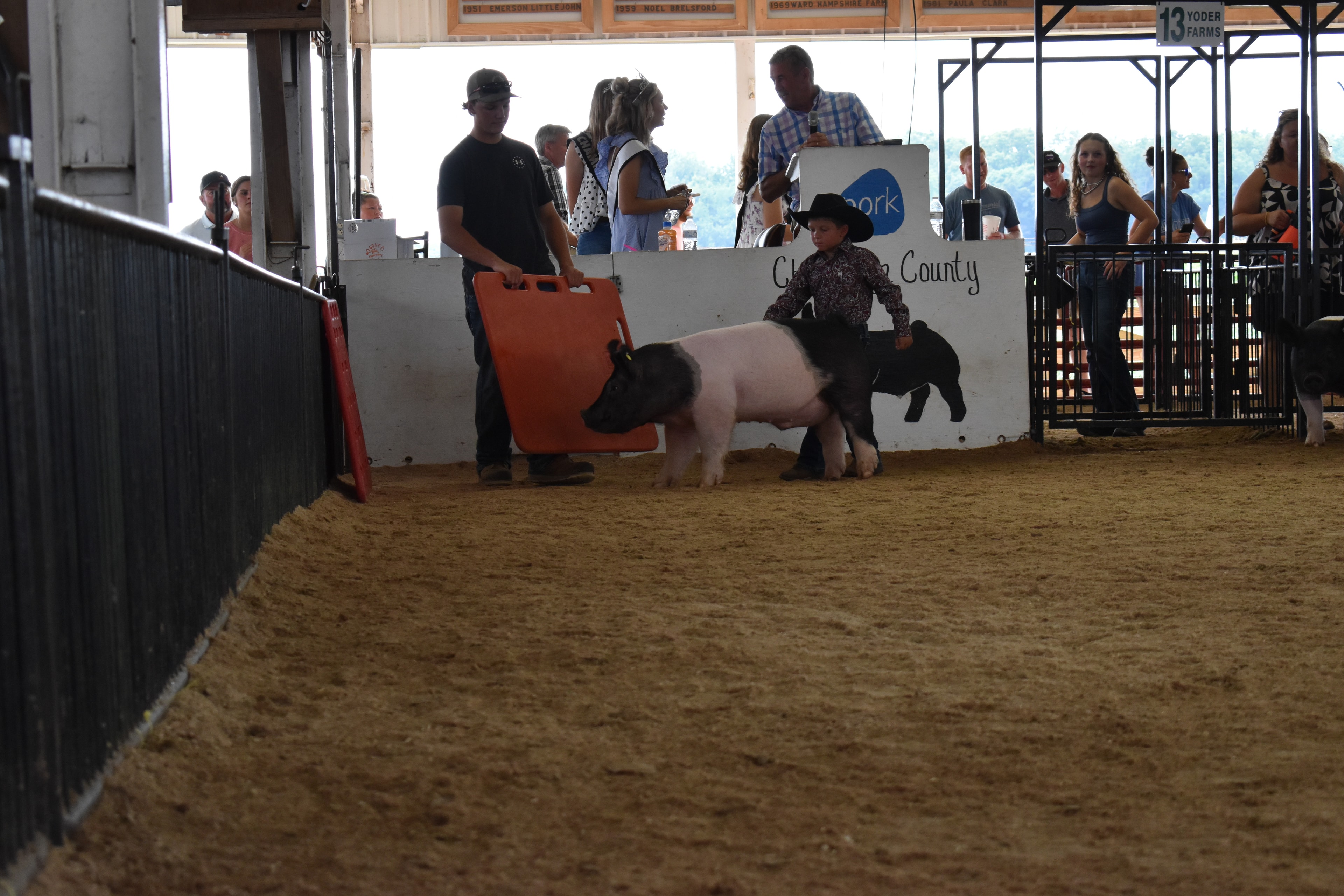 Small boy in black cowboy hat steering Hampshire cross pig with girl in black turtleneck and large Hampshire cross pig in foreground