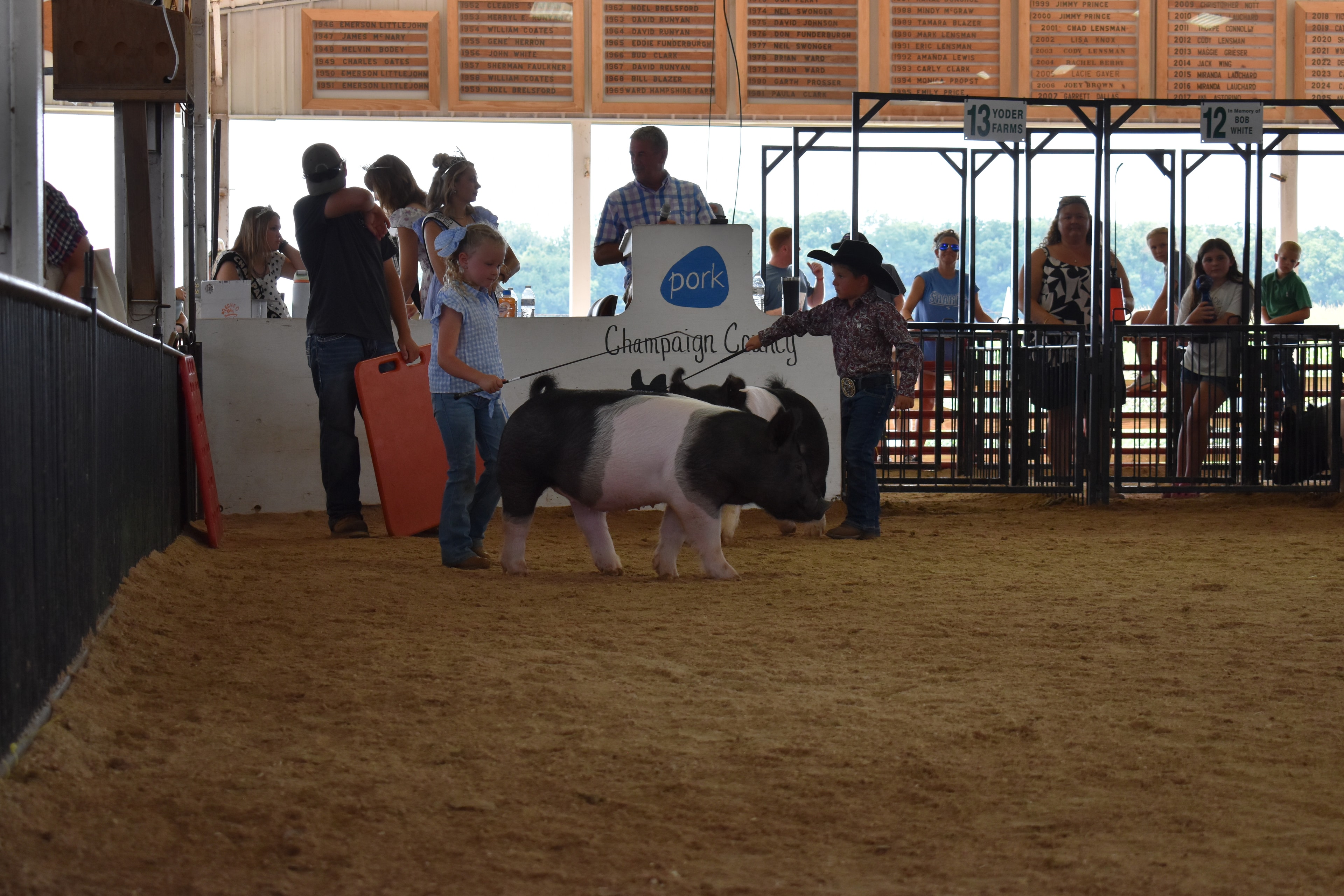 Small boy in black cowboy hat steering Hampshire cross pig with Champaign County Pork sign and Pork Queen with sash in background
